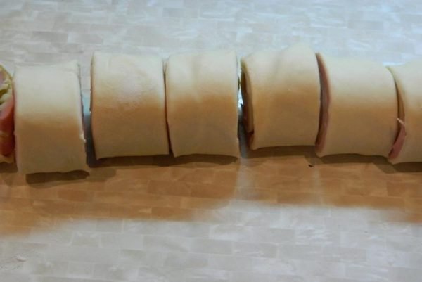 Нарезанный порционными кусочками рулет из сырого теста с колбасой и сыром на столе